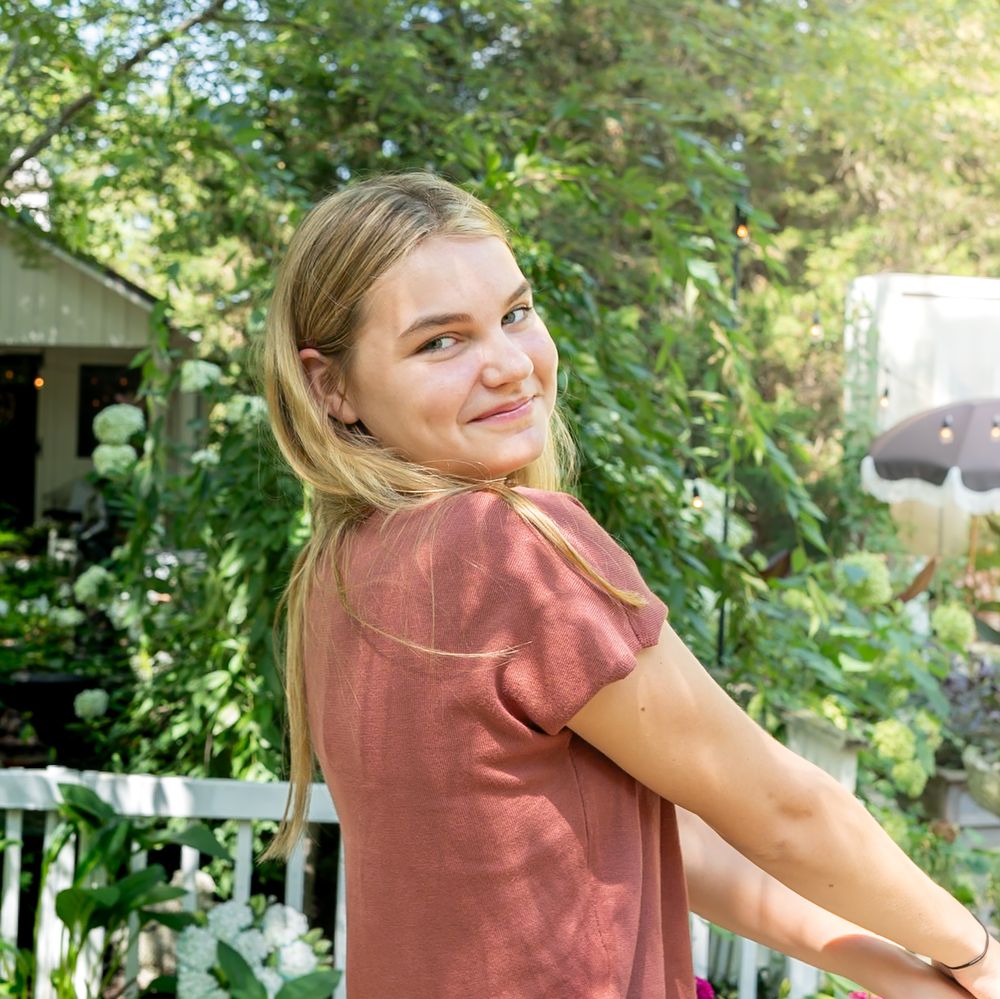 Person in a coral colored shirt enjoying a sunny day on an outdoor porch.