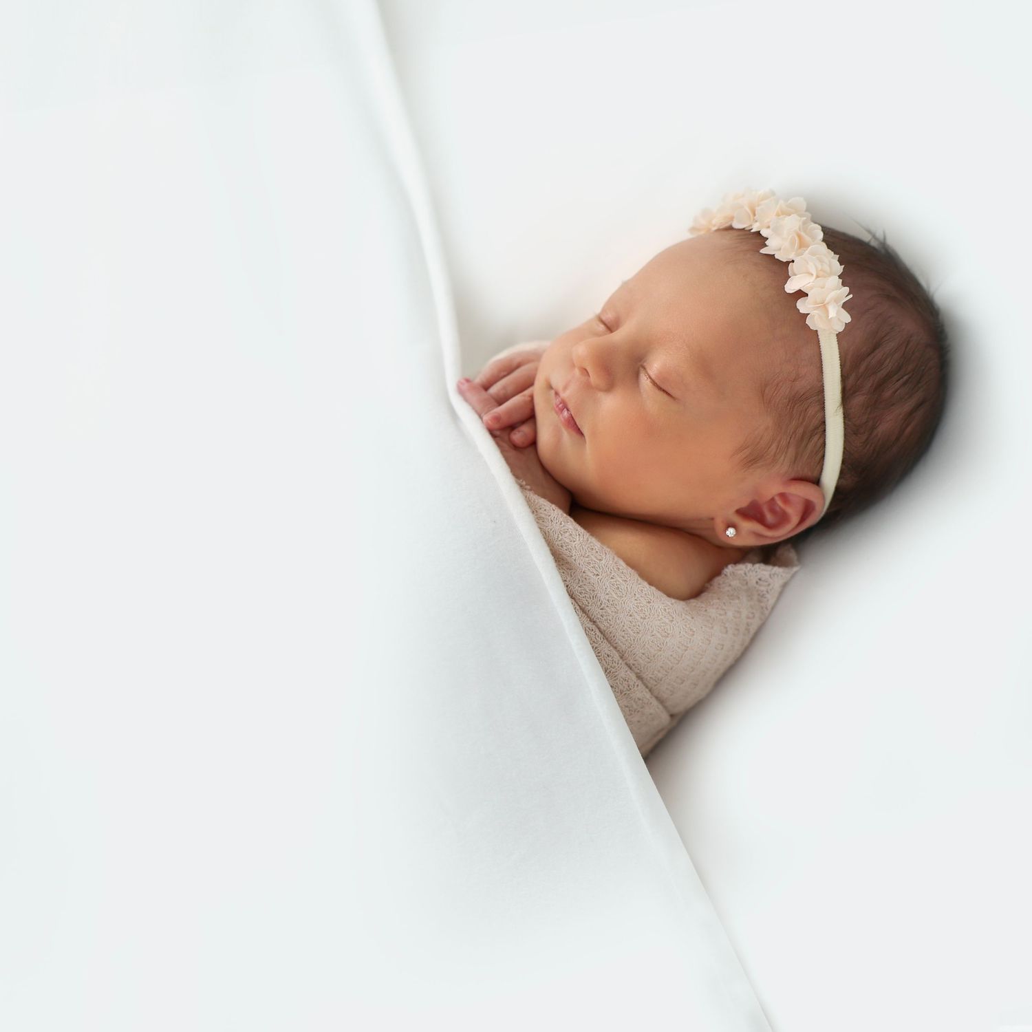 peacefully sleeping newborn with a floral headband and her little fingers peeking out from under a blanket
