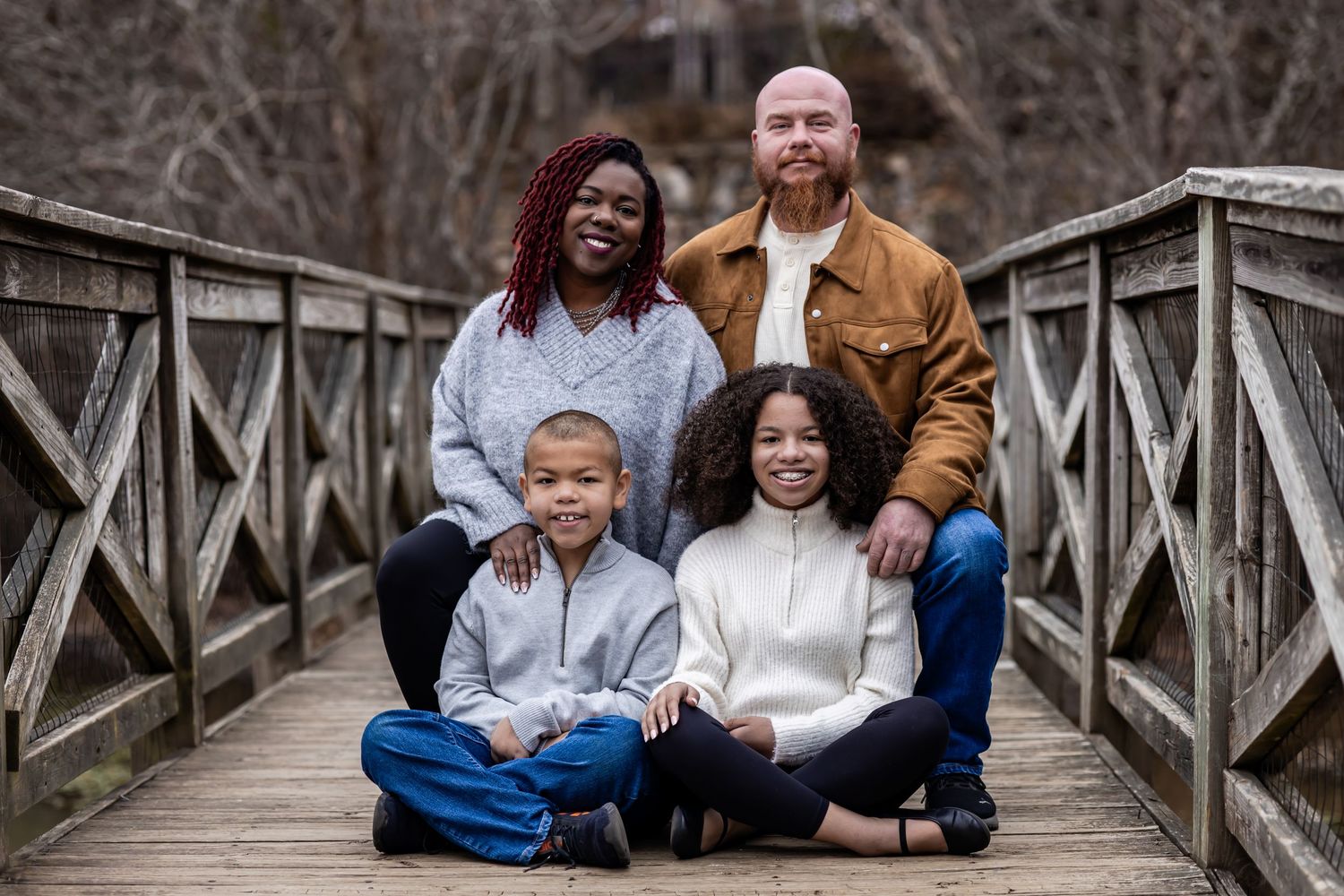 A happy family sits together on a wooden bridge during an outdoor photo session.