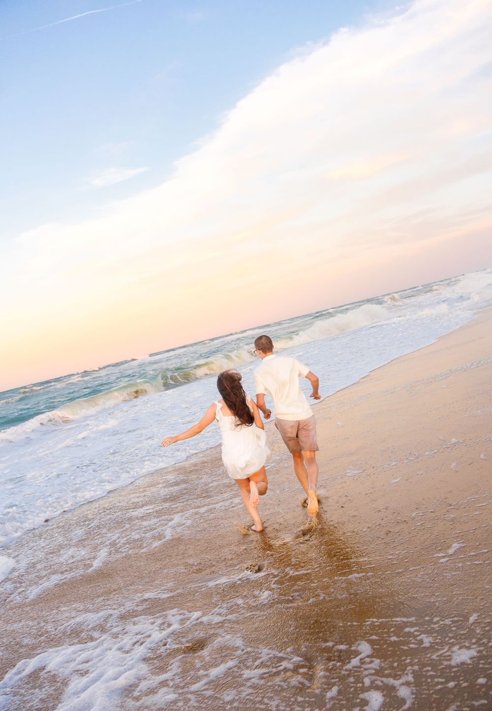 Couple running hand-in-hand along a sandy beach at sunset, waves gently lapping at their feet.