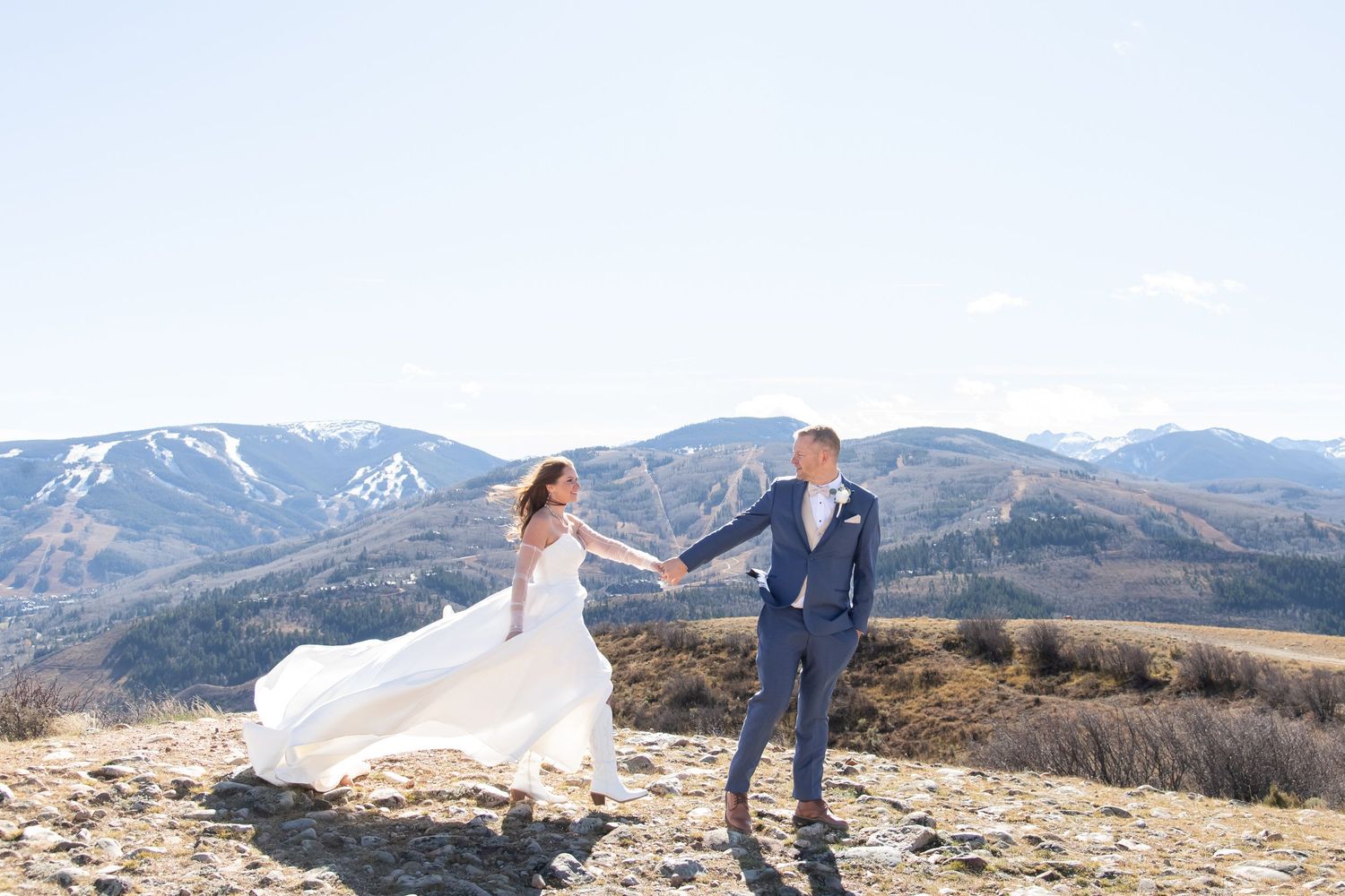 bride and groom stands on mountain summit with scenic snow-capped peaks and valley views in background for beaver creek wedding