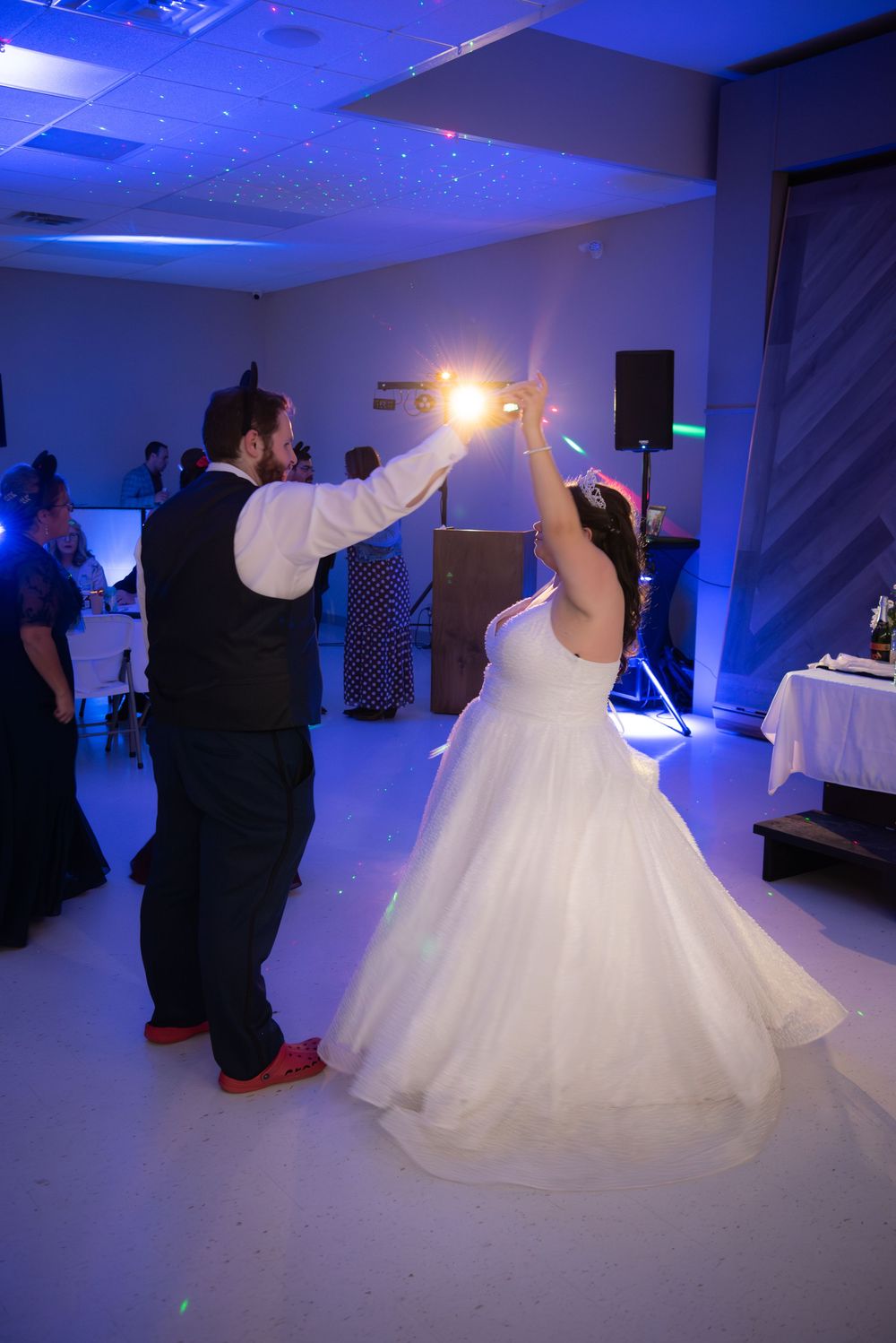 Newlyweds share their first dance in a ballroom illuminated with blue lighting and white decor.