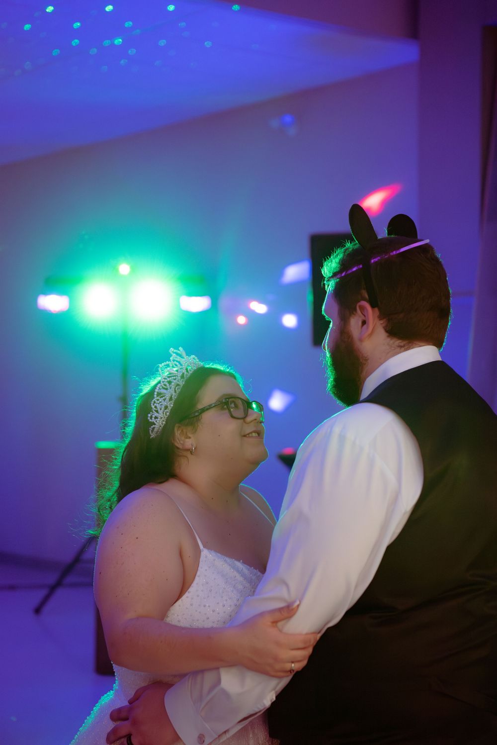 A couple shares a romantic dance moment under blue and green lighting at their wedding reception.