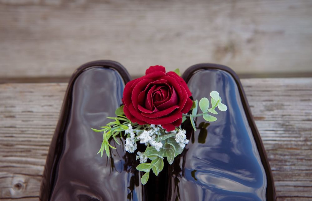 A row of brown leather dress shoes decorated with red roses and green foliage on rustic wooden planks.