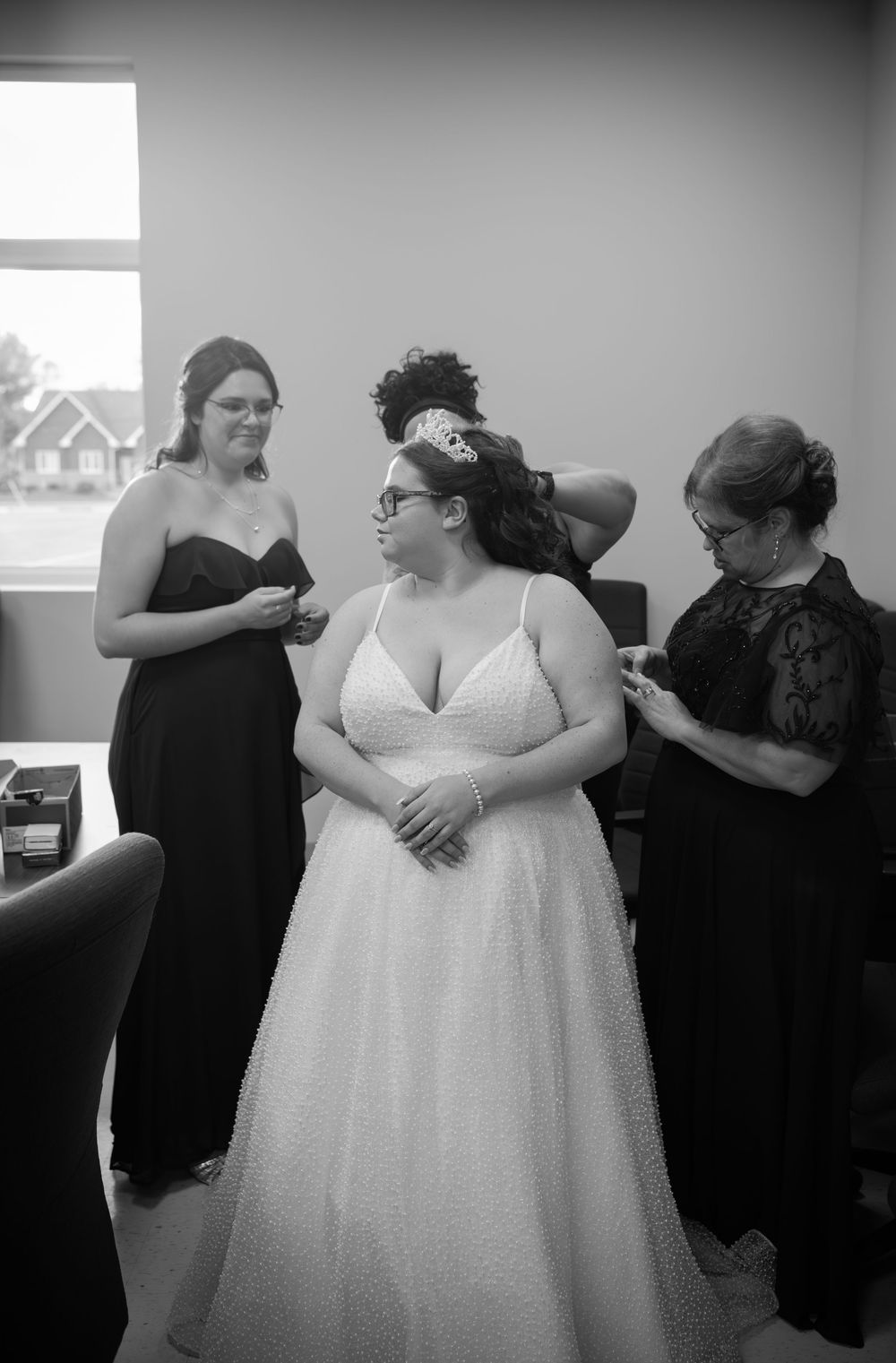 Wedding preparations showing attendants in black helping with a white wedding dress.