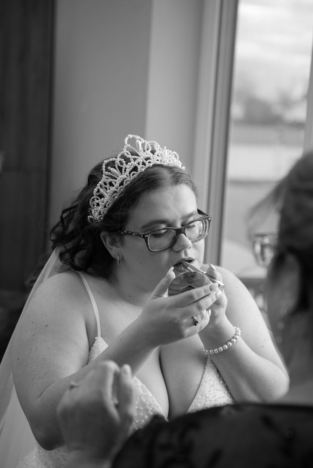 A bride in a white dress and tiara takes a bite of food during what appears to be her wedding reception.