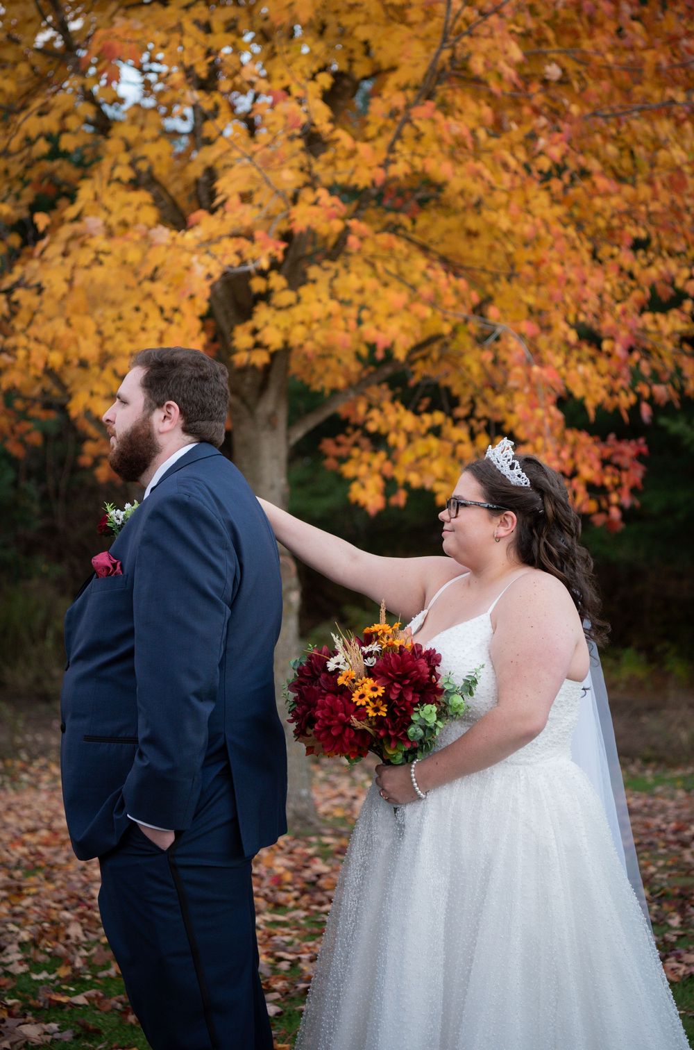 Couple shares a romantic first look moment surrounded by vibrant orange fall foliage in the background.