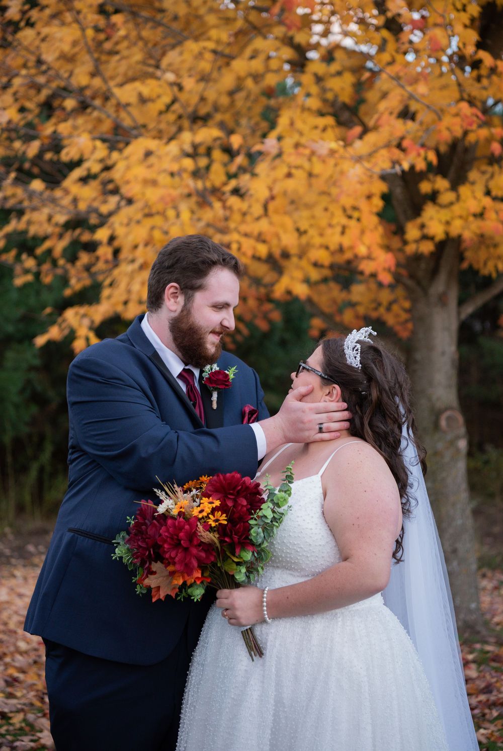 Newlywed couple shares romantic kisses under vibrant autumn foliage in a beautiful outdoor fall wedding scene.