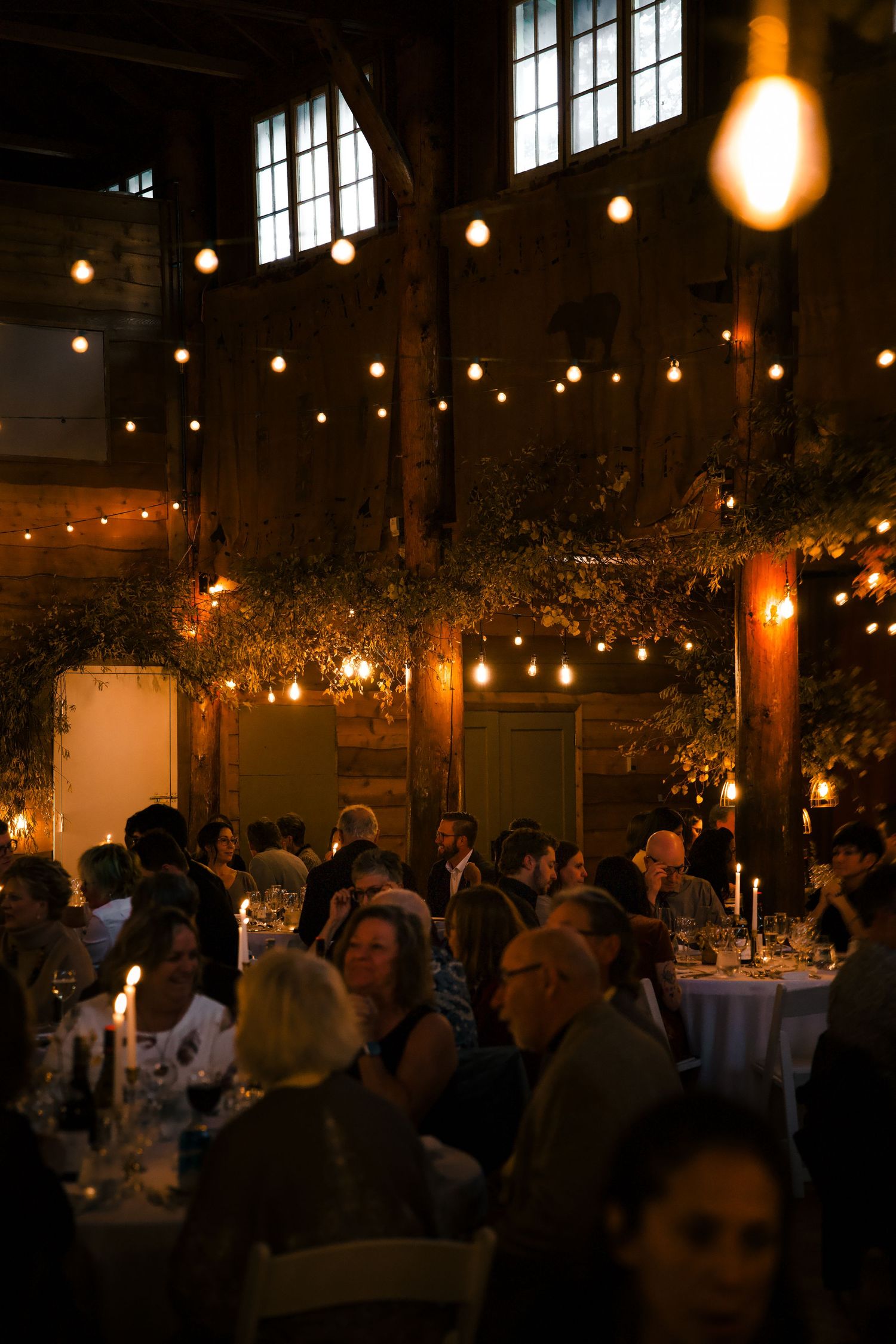 Dimly lit banquet hall filled with guests beneath twinkling lights and wooden beams.