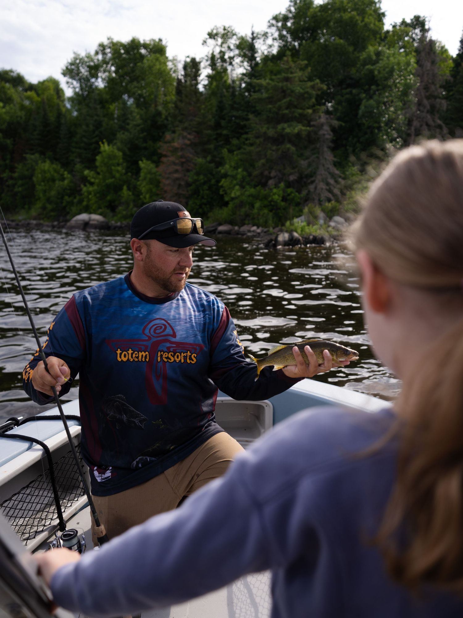 Group fishing from a boat on a tranquil lake surrounded by trees.