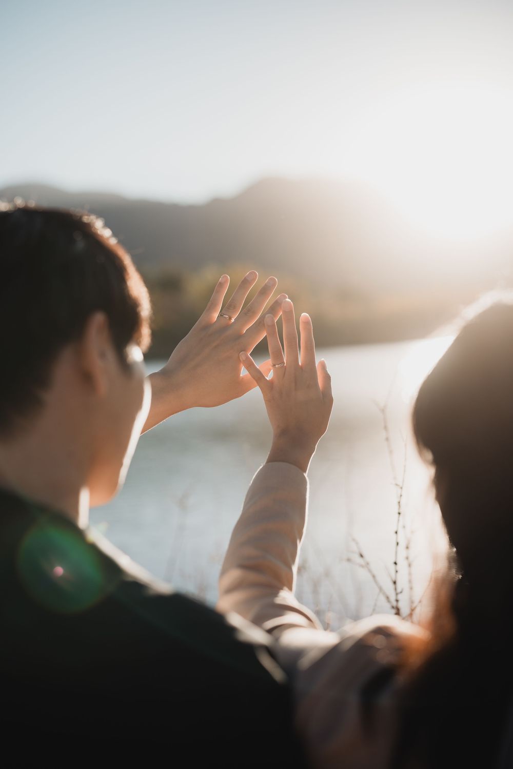 Silhouetted hands reach up against bright sunlight creating a dreamy atmospheric scene at sunset.