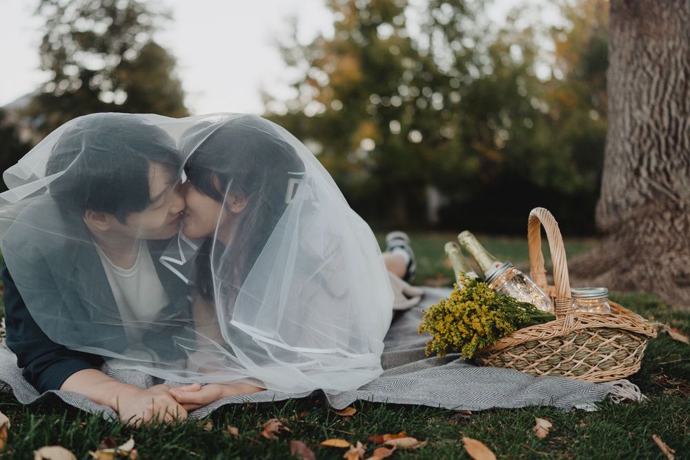 A romantic wedding couple shares intimate moments under a flowing veil in an outdoor garden setting.