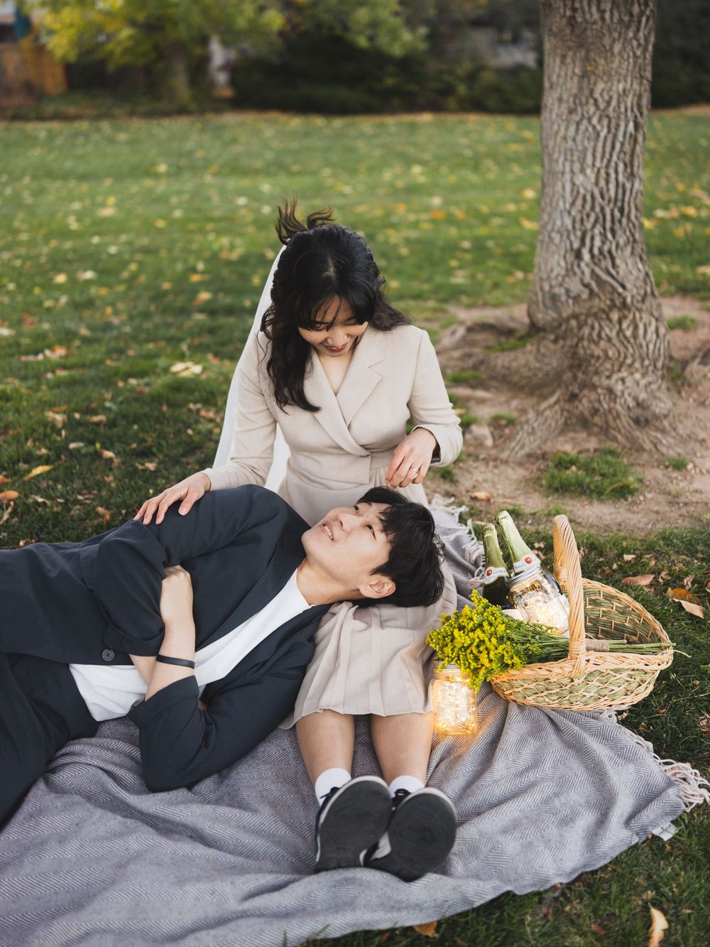 A couple shares a romantic moment while resting on a gray blanket under trees during an autumn picnic.