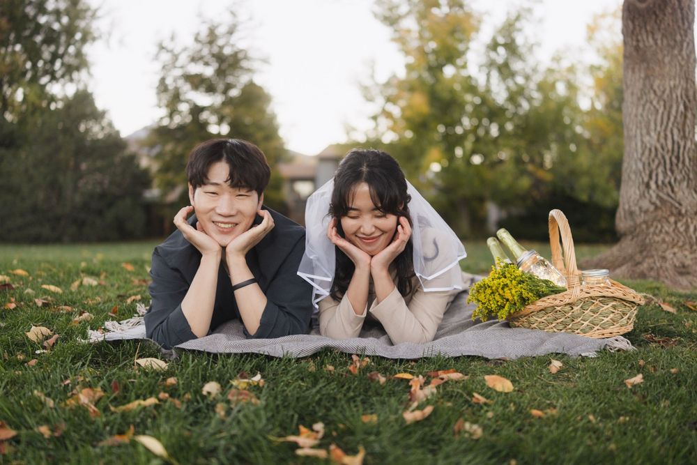Two people lying on grass with autumn leaves in a park during golden hour.