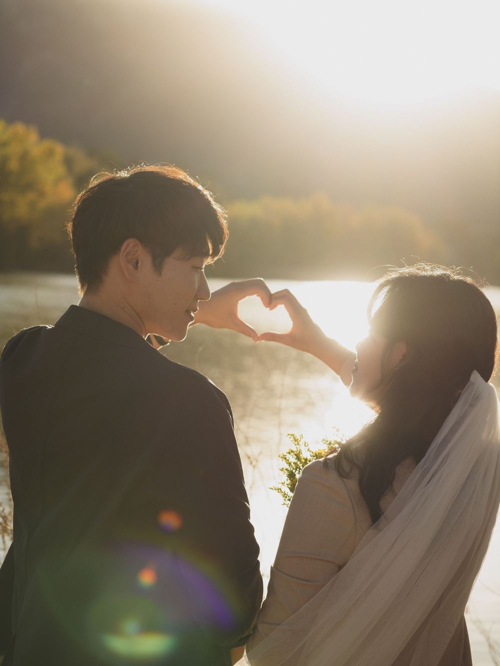 Silhouetted couple embraces against golden sunlight during sunset photoshoot by the water.