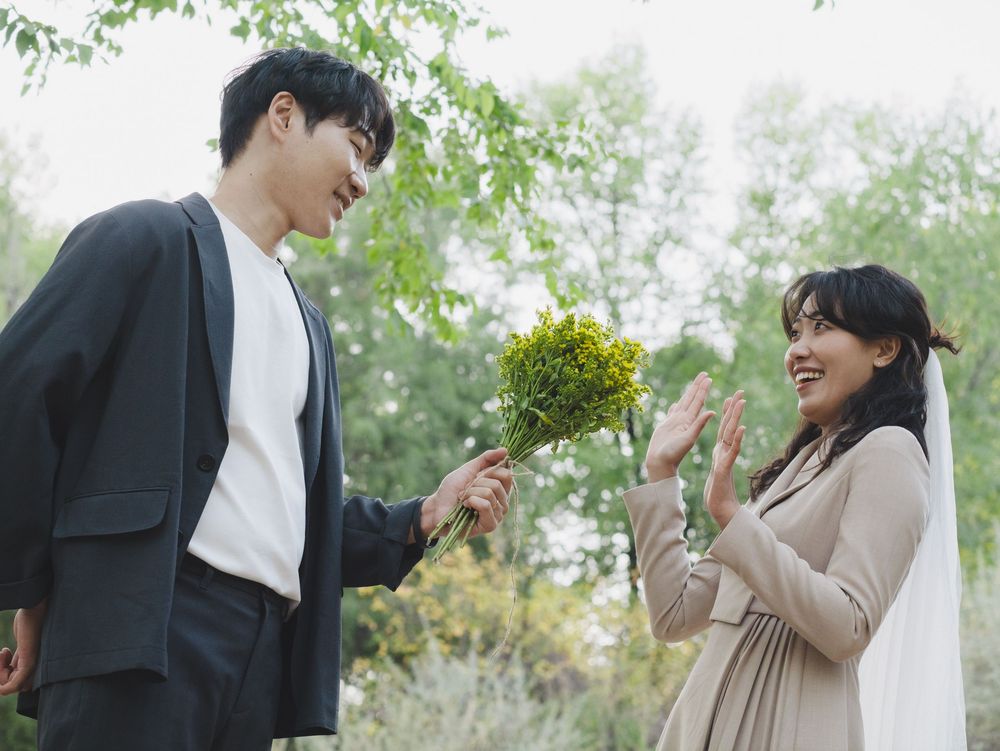A couple in formal attire shares a romantic moment in a lush garden setting with blooming flowers and greenery.