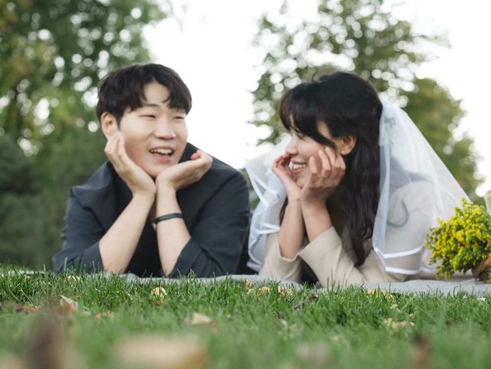 A couple lies on grass outdoors in a romantic photoshoot setting wearing black and white attire.