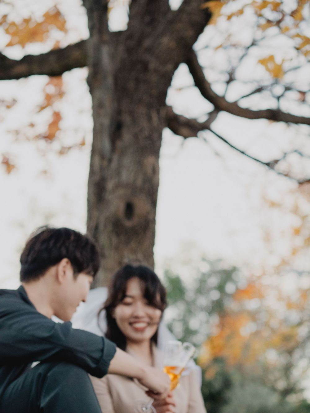 Couple shares joyful moments under autumn trees with falling leaves in natural outdoor setting.