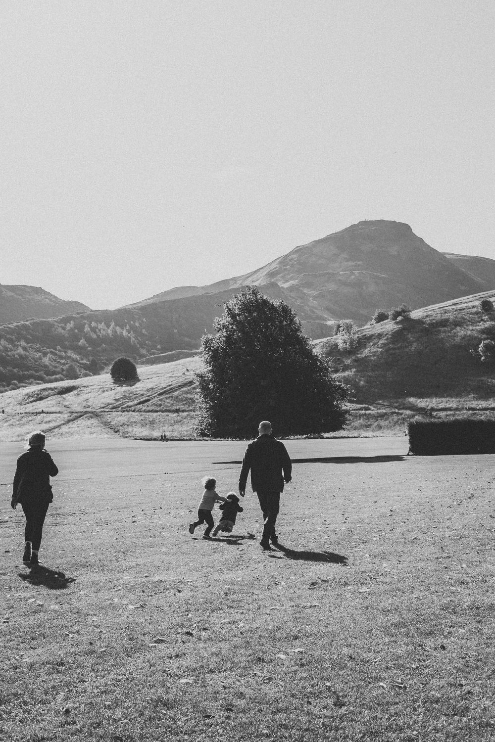 Silhouettes of people walking together on a grassy field with mountains in the background on a sunny day.