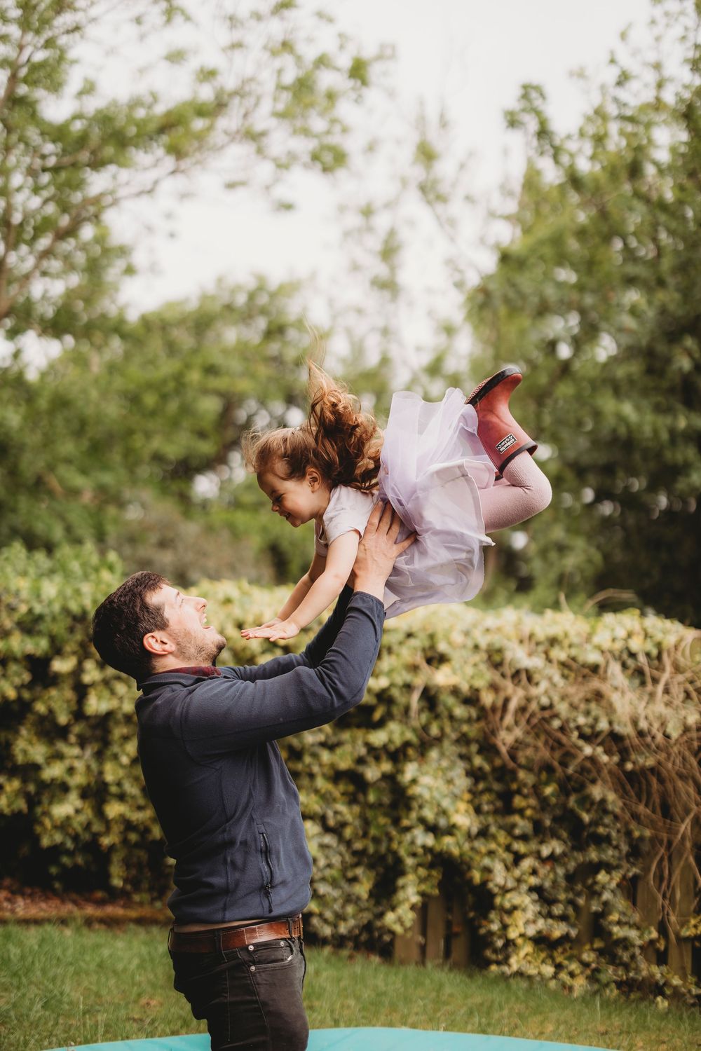 A sequence of joyful moments showing a parent tossing a child in the air against a green garden backdrop.