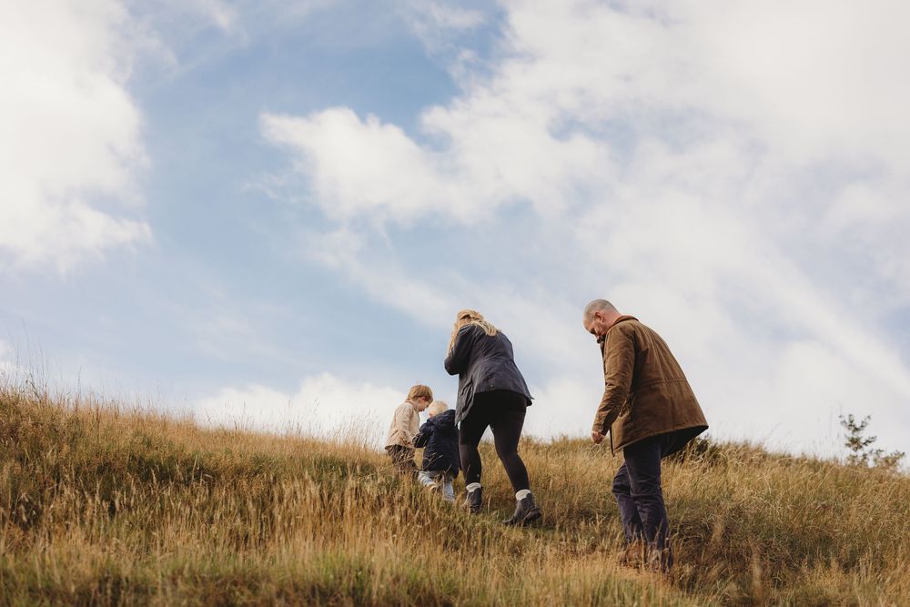People hiking together on a grassy hillside under a bright blue sky with white puffy clouds.