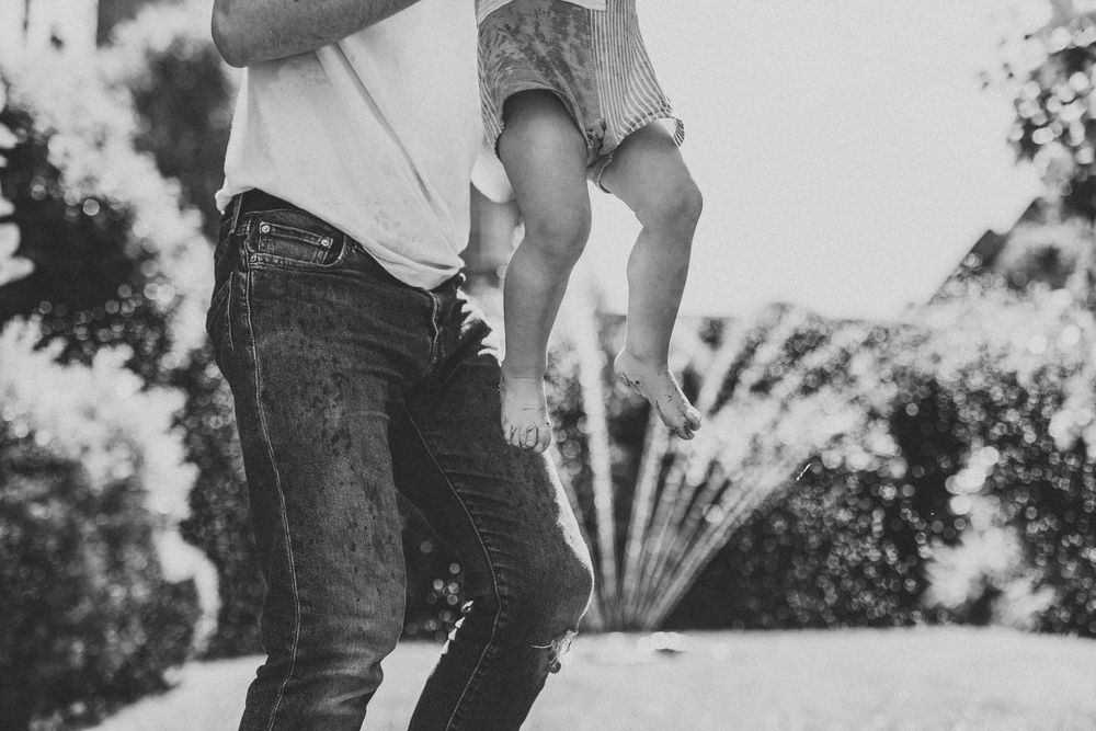 Candid monochrome capture of outdoor water play moments in a garden setting.