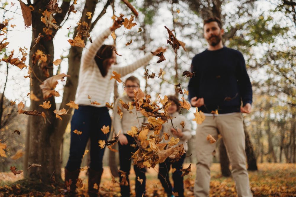 People throwing autumn leaves in the air at sunset in a forest during a joyful outdoor photoshoot.