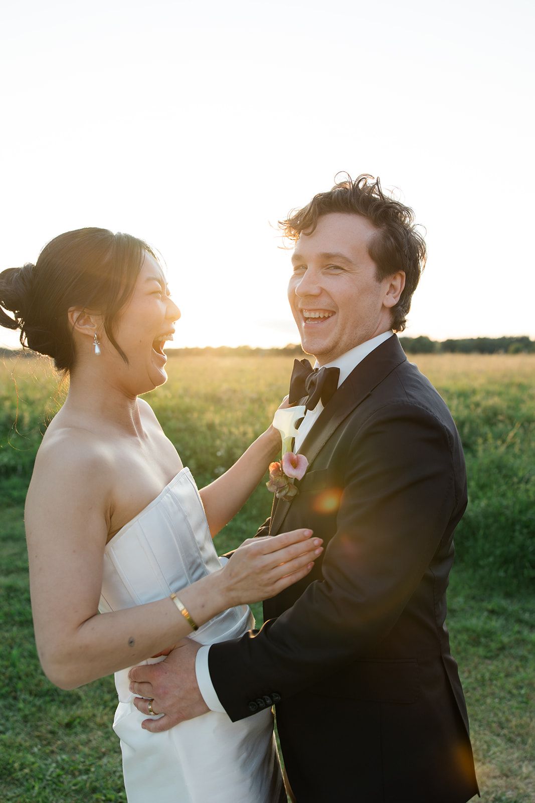 A couple in wedding attire shares playful moments together in a sunlit field during golden hour.