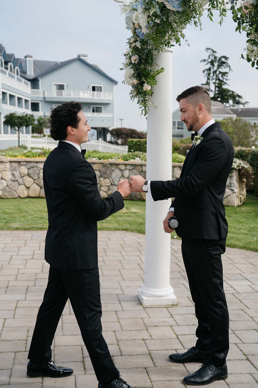 Two people in formal attire playfully engage in a mock fight sequence on an outdoor stone patio near white columns.