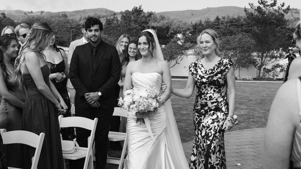 Black and white panoramic shot of wedding guests gathered at an outdoor venue with white chairs.