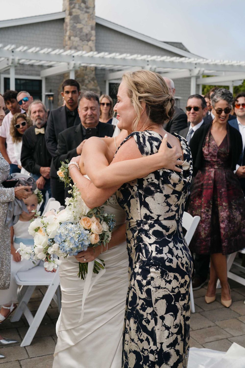 Wedding guests and wedding party gathered on a decorated outdoor patio with floral arrangements.