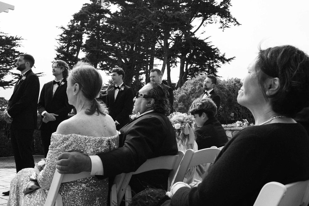 Wedding ceremony audience seated in white chairs watching the proceedings outdoors.