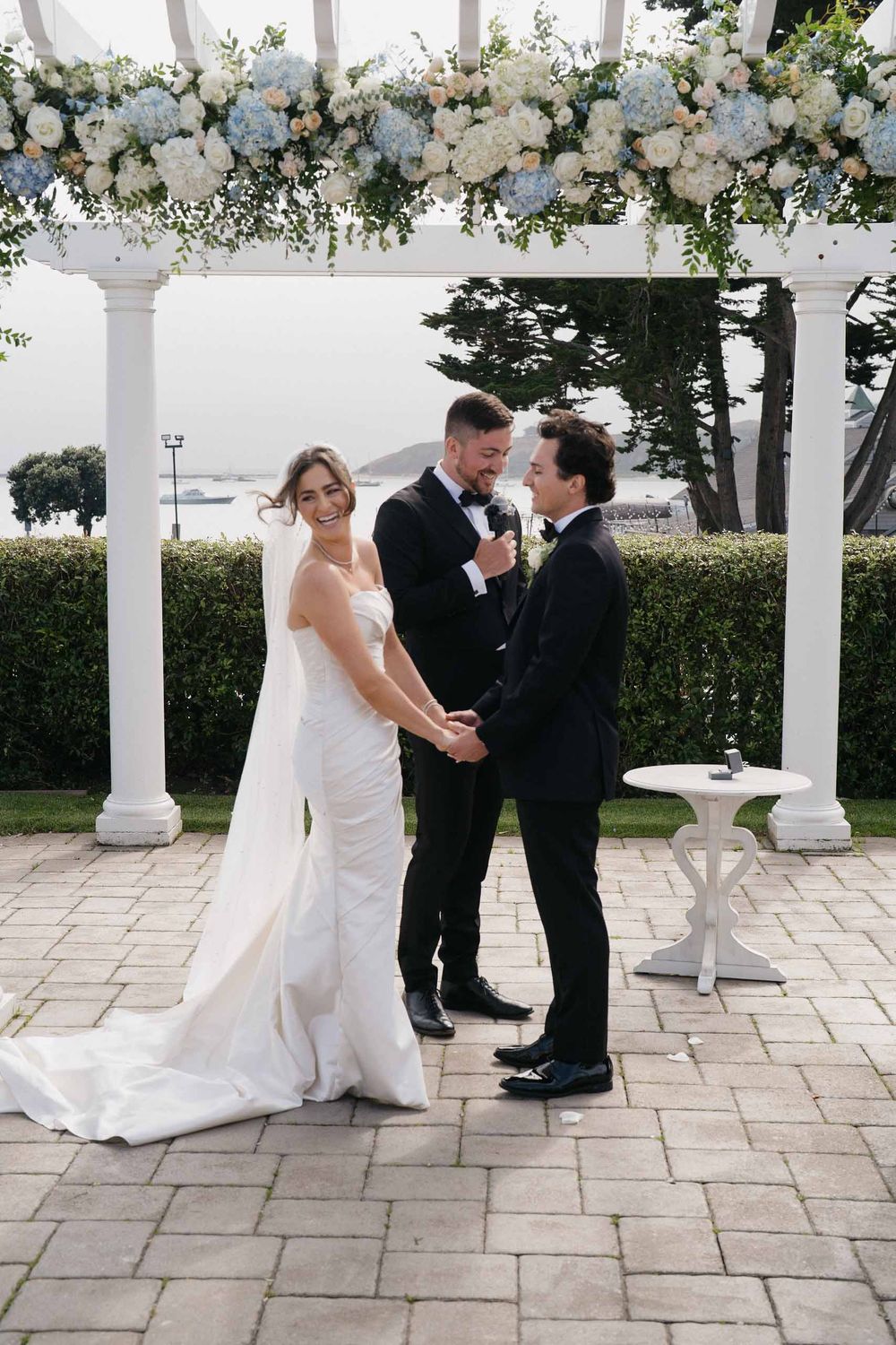 Wedding ceremony under a white pergola decorated with elegant white floral arrangements.