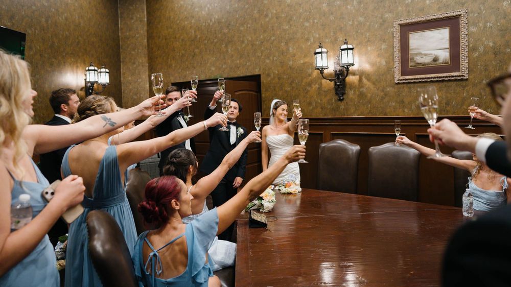 A panoramic view of people dancing and celebrating in a rustic wood-paneled reception hall with lantern lighting.