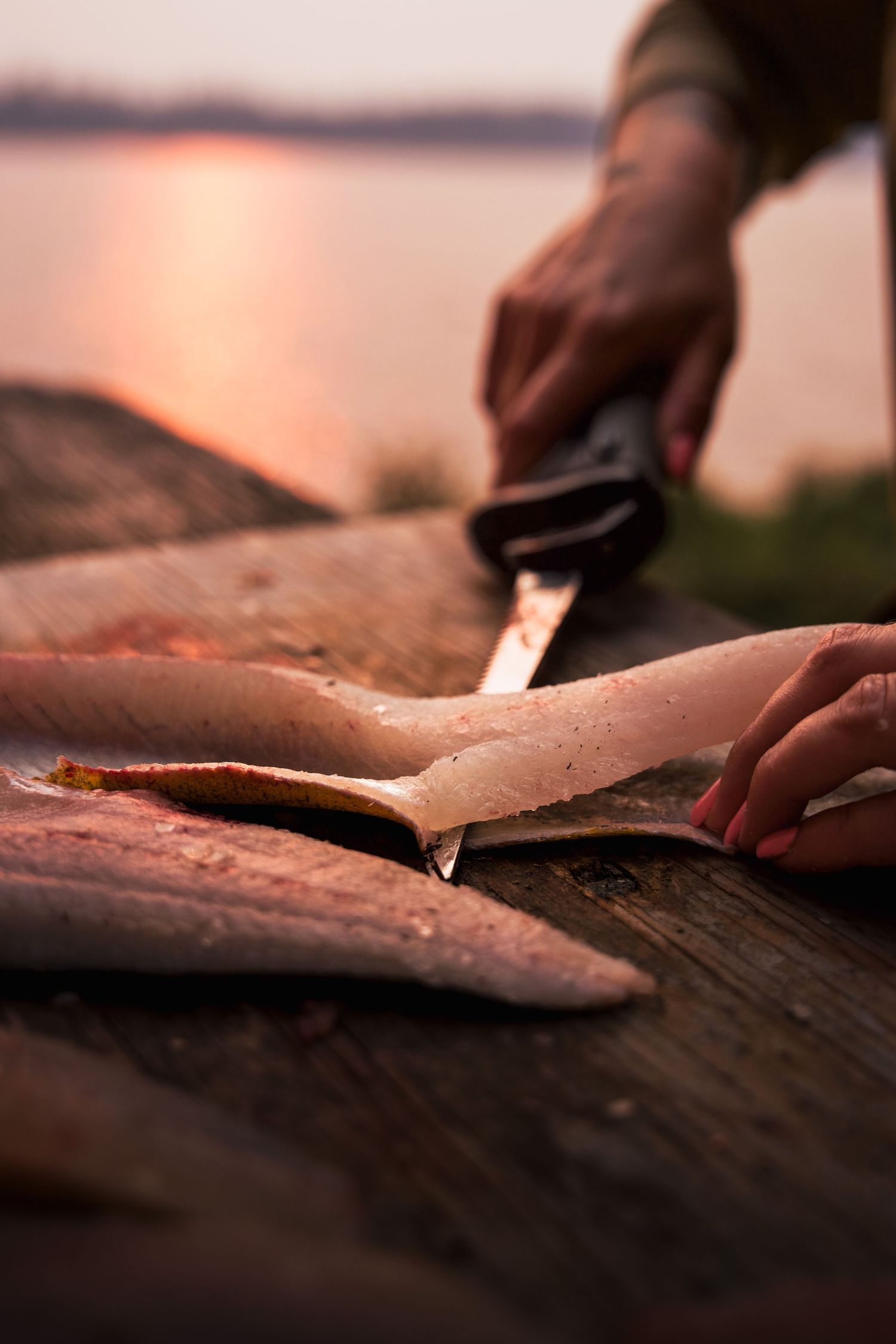 Fresh fish fillets being prepared on a wooden cutting board at sunset.