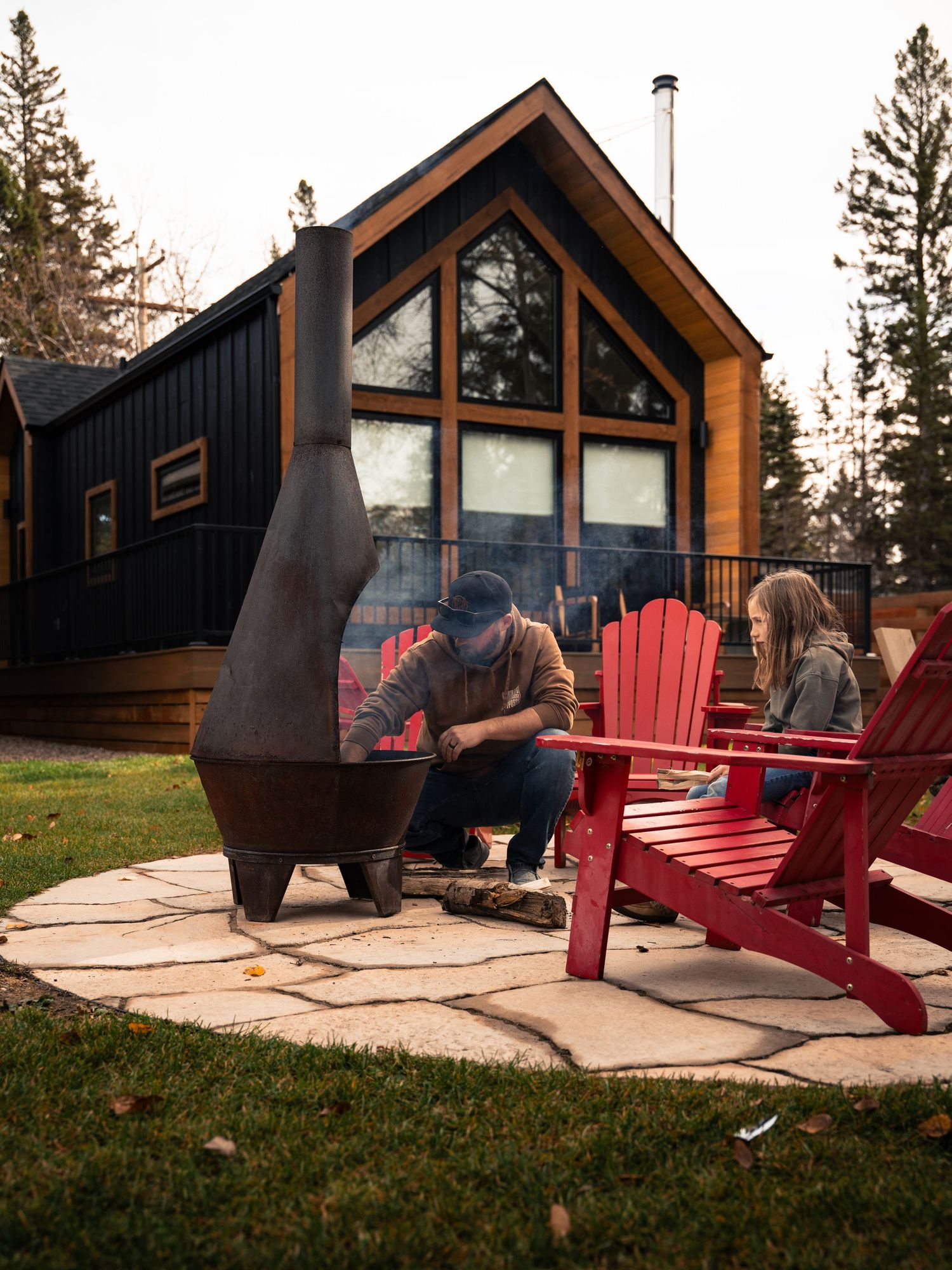 Modern wooden cabin with red Adirondack chairs on the patio at sunset.