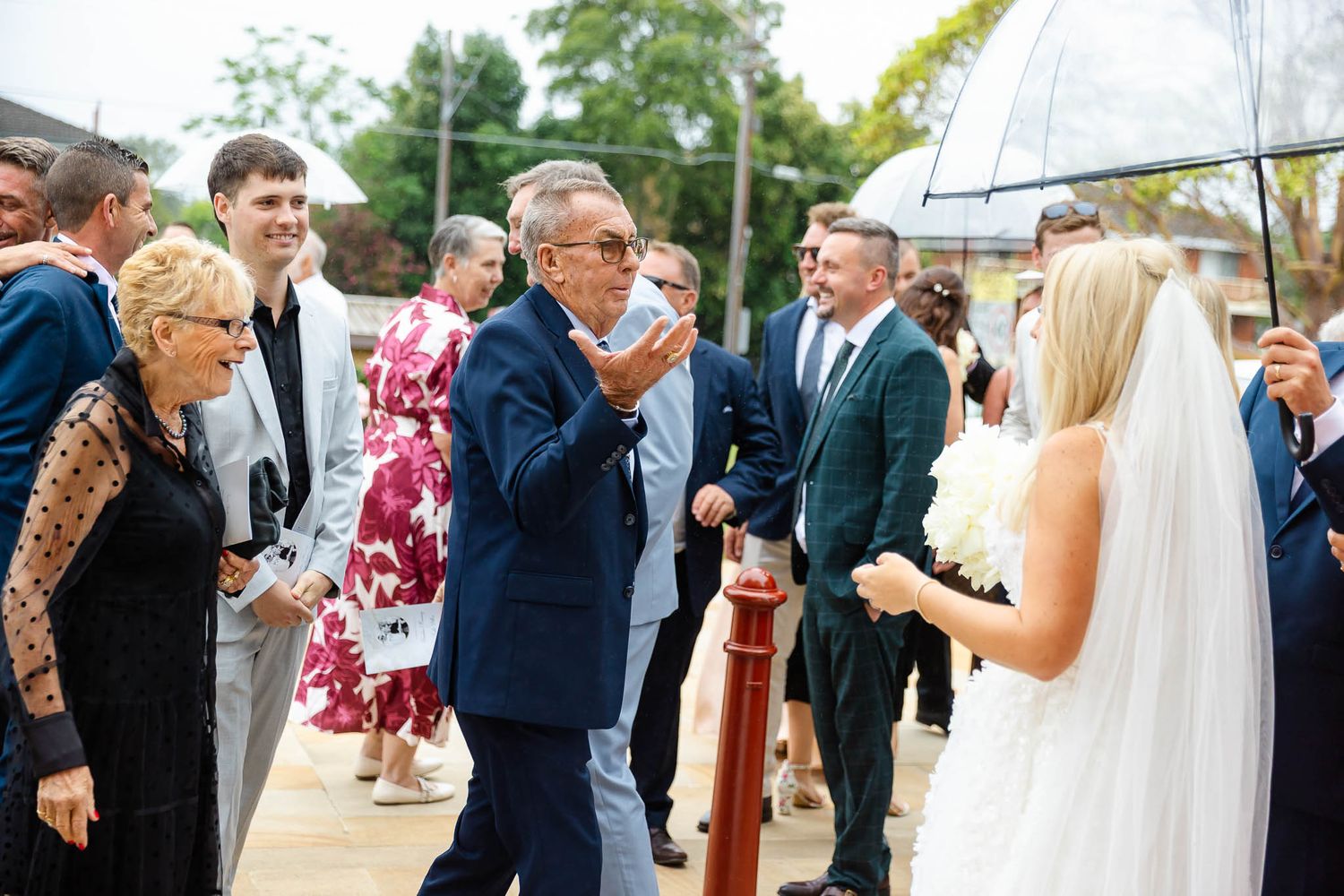 Wedding guests gather outdoors to celebrate with the bride in her flowing white veil during a summer celebration.