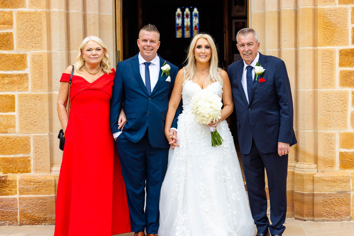 Wedding party poses together outside a stone church building with elegant gothic windows and architecture.
