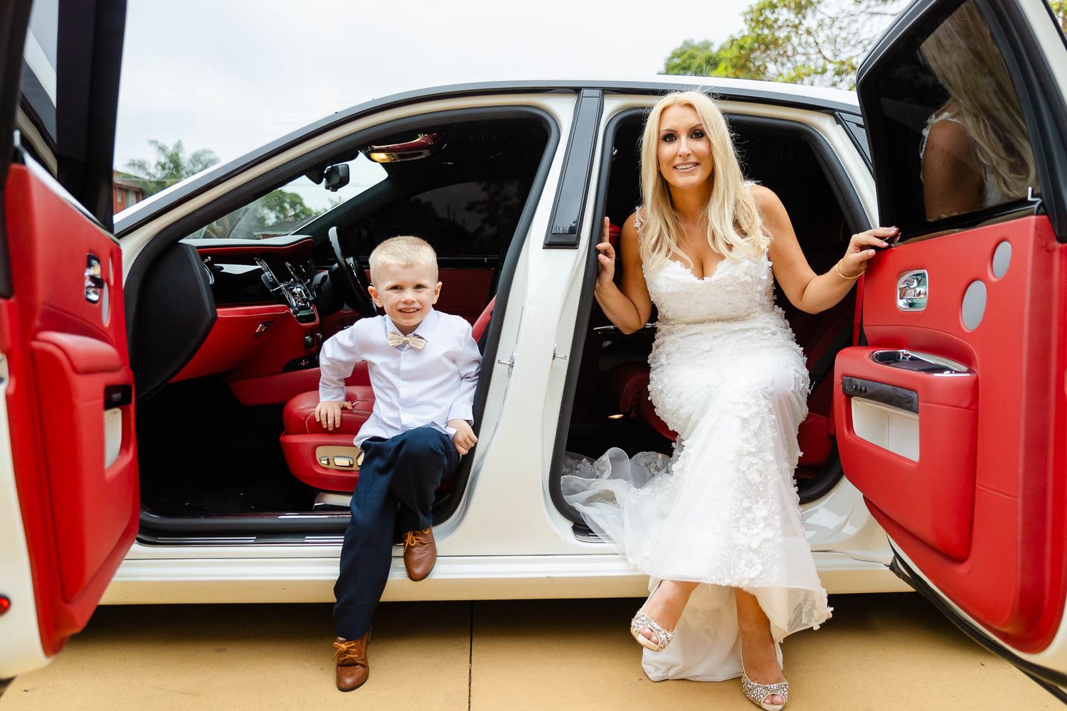 A white luxury car with red interior and open doors parked outdoors on a sunny day.