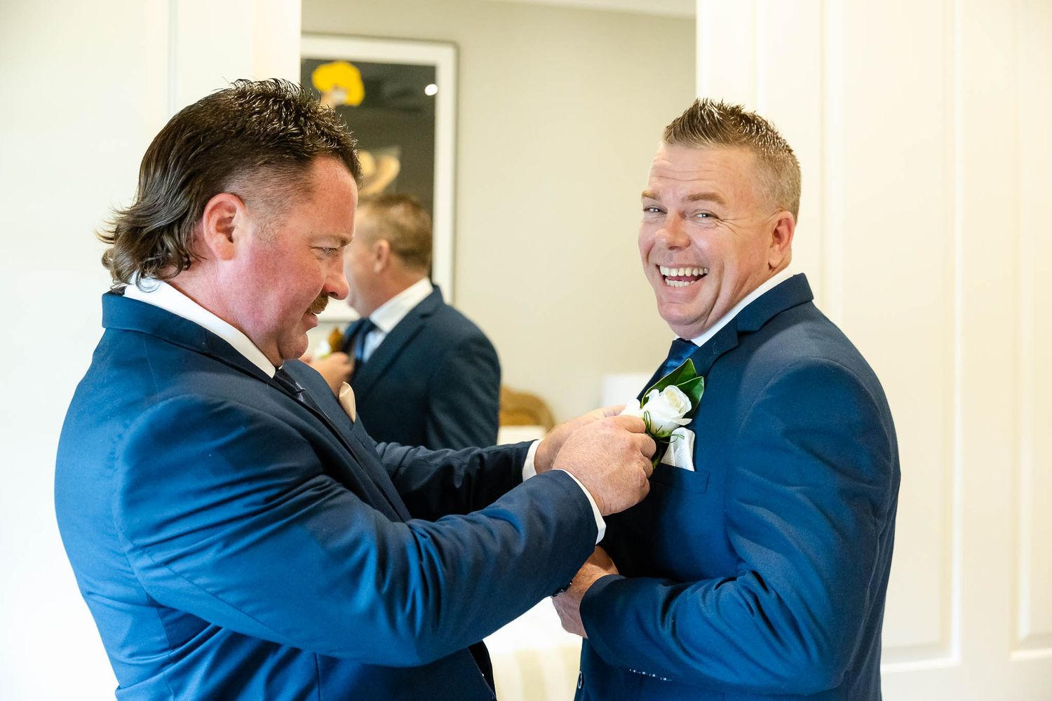 Two people in navy suits share a joyful moment while laughing together in a bright indoor setting.