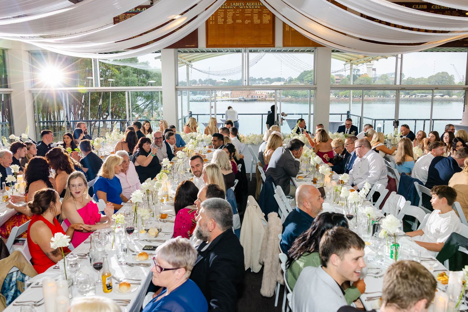 Panoramic view of a bright wedding reception venue filled with guests dining at decorated tables.