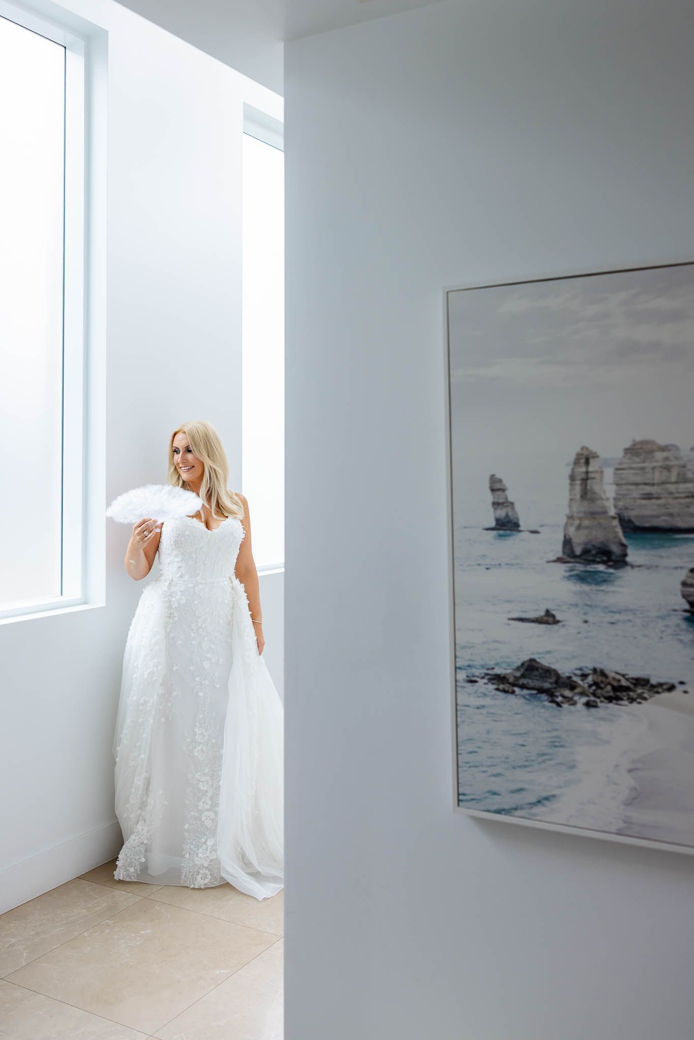 A minimalist white gallery space with coastal artwork and a flowing white dress creating an ethereal atmosphere.
