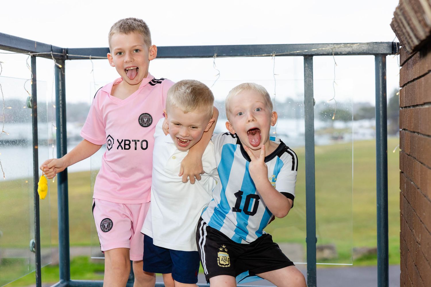 Children excitedly look through glass windows at a scenic outdoor view during a sunny day.