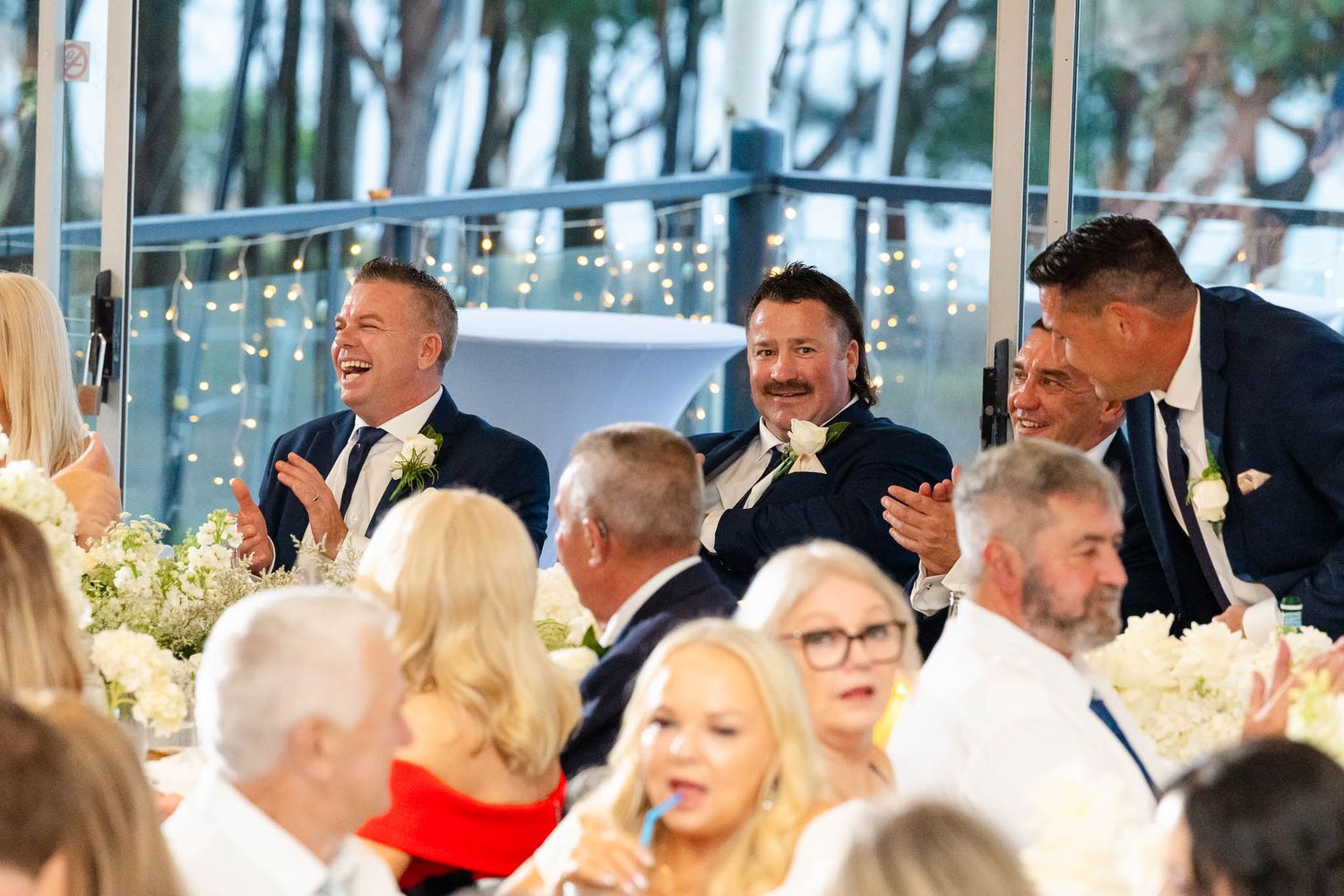 Wedding reception guests seated at decorated tables in an elegant venue with twinkling lights and floral arrangements.