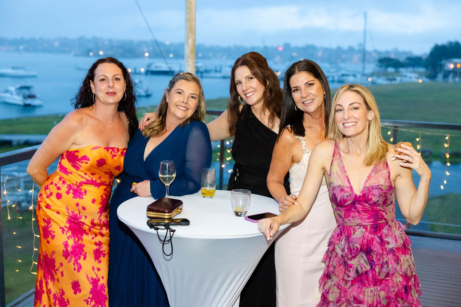 A group of friends enjoying drinks and conversation at a cocktail party overlooking a scenic waterfront view.