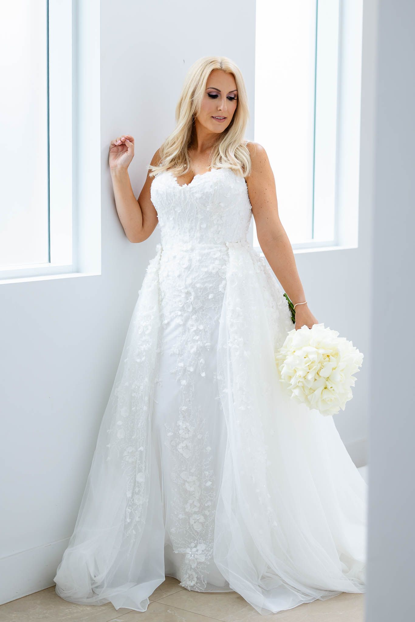 Elegant plus size wedding gown with lace details and flowing tulle skirt shown with white floral bouquet.