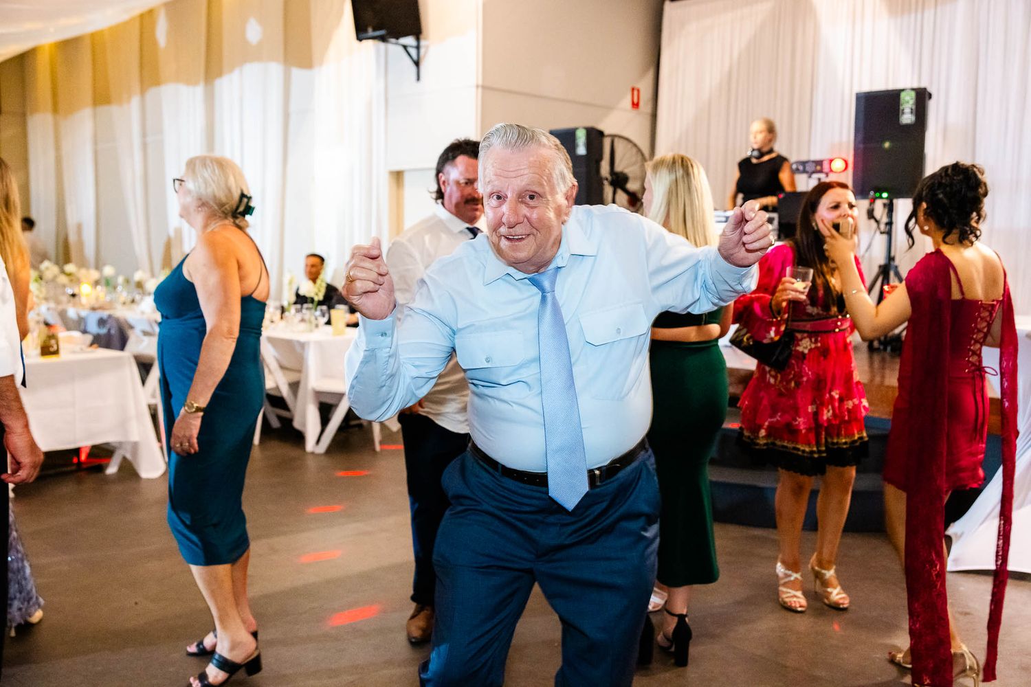 Guests dancing and celebrating on a brightly lit dance floor at an elegant indoor wedding reception.