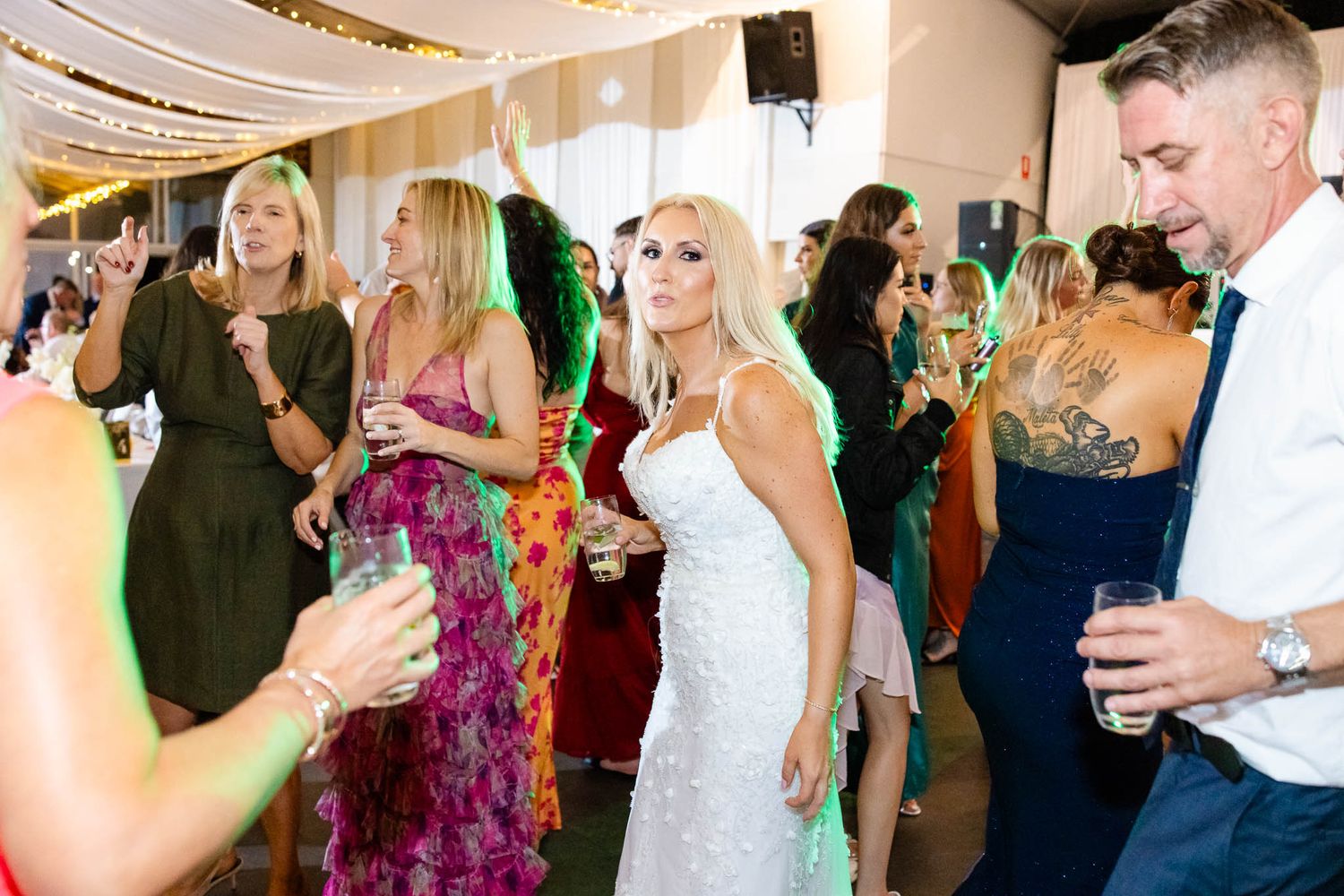 Wedding guests mingle and socialize during a lively reception celebration at an indoor venue.