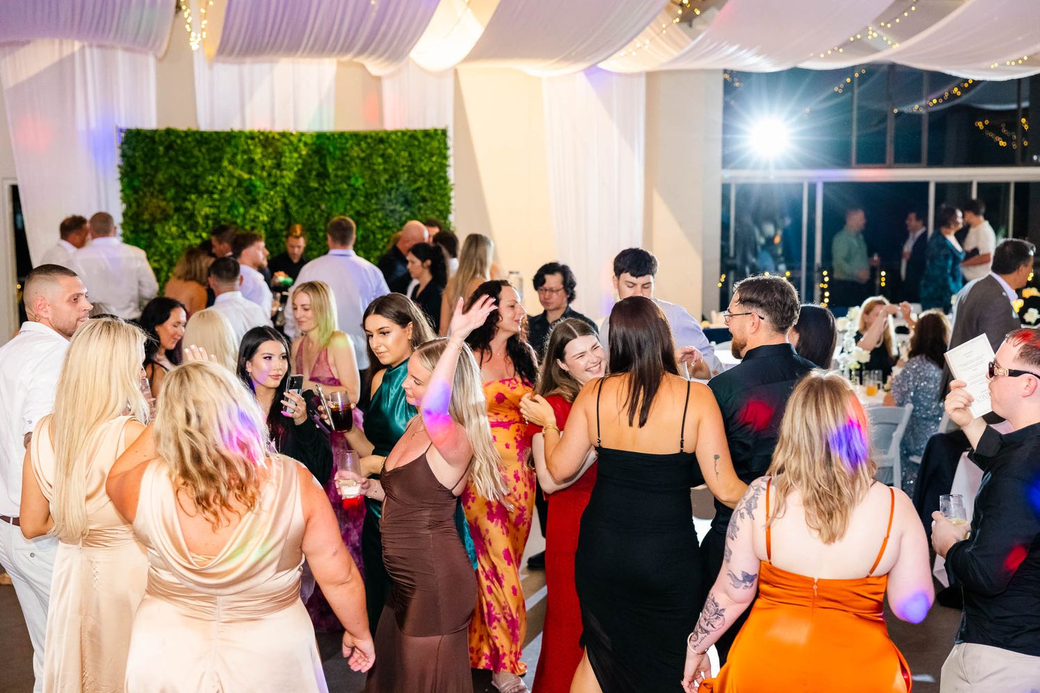 A lively dance floor filled with party guests dancing and celebrating under a white tent canopy.
