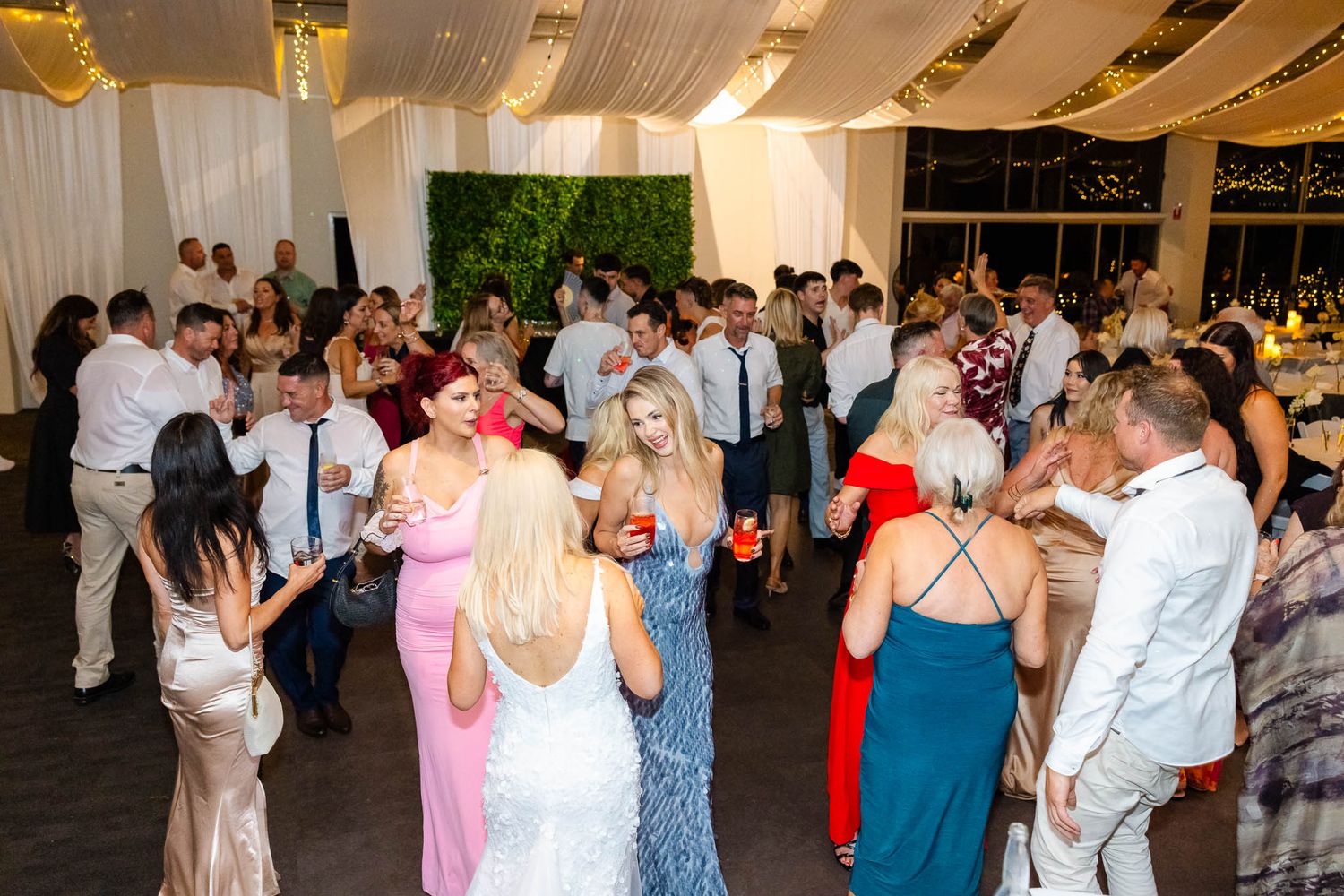 Wedding reception guests dancing together on a decorated dance floor during an evening celebration.